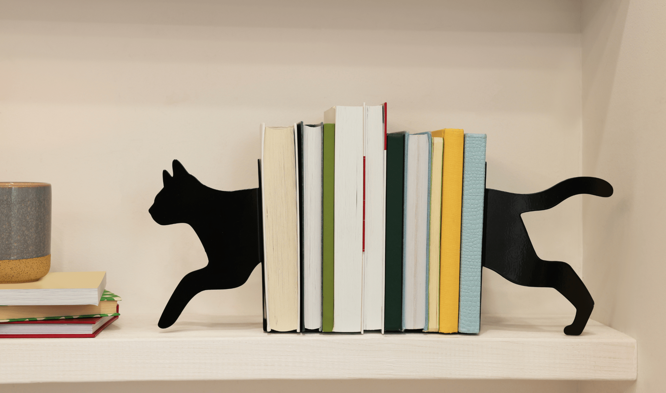 Some books on a bookshelf with bookends that look like a black cat walking through them.