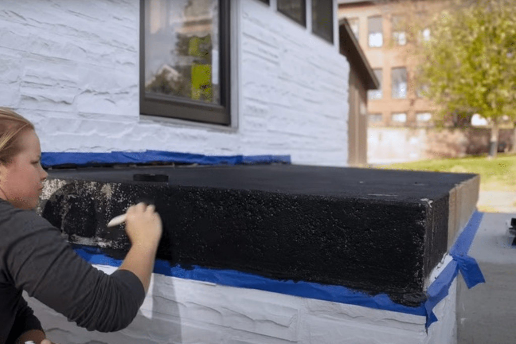 A woman painting over a box outdoors with textured black paint.