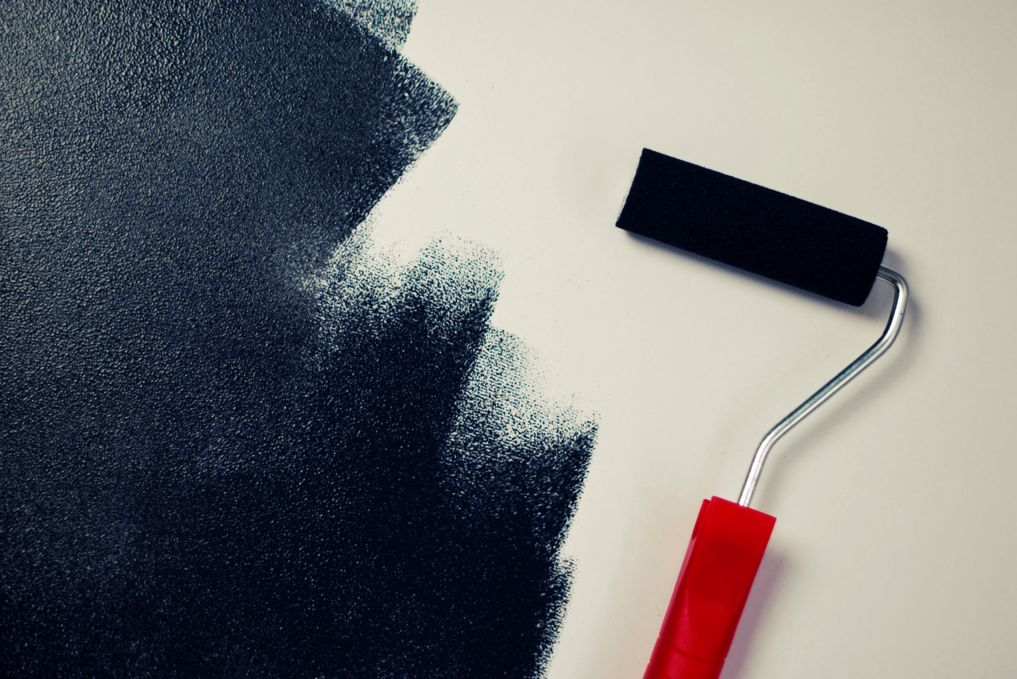 A navy blue paint roller next to a half-painted wall.