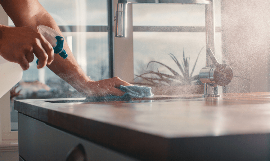 Someone spraying down a counter with a cleaner, rag in the other hand wiping it all down.