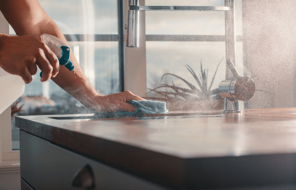 Someone spraying down a counter with a cleaner, rag in the other hand wiping it all down.