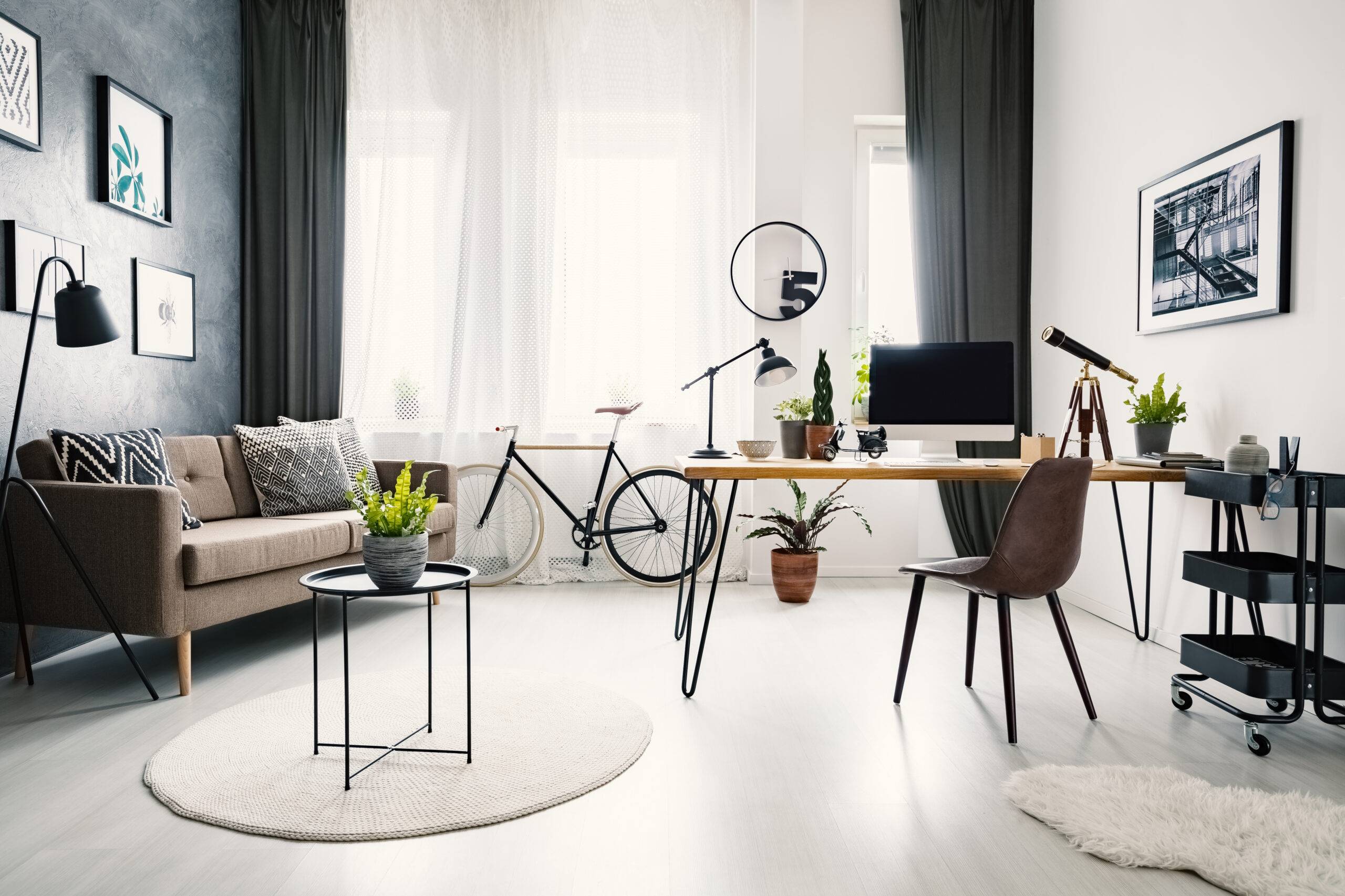 Black chair at wooden desk with desktop computer in workspace interior with sofa and bike. Real photo