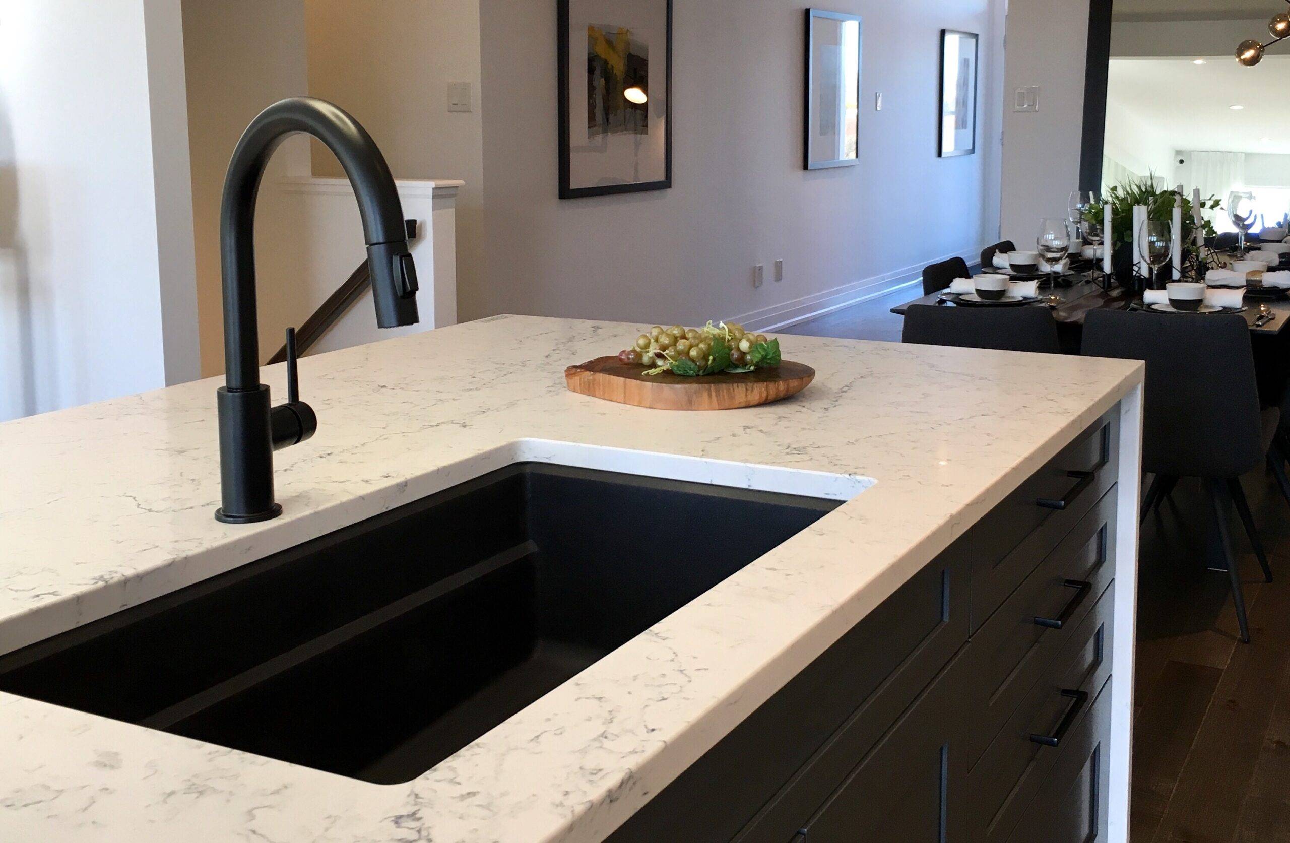 A white marble-like countertop on a kitchen island atop some black cabinets, a black sink fitted into it.