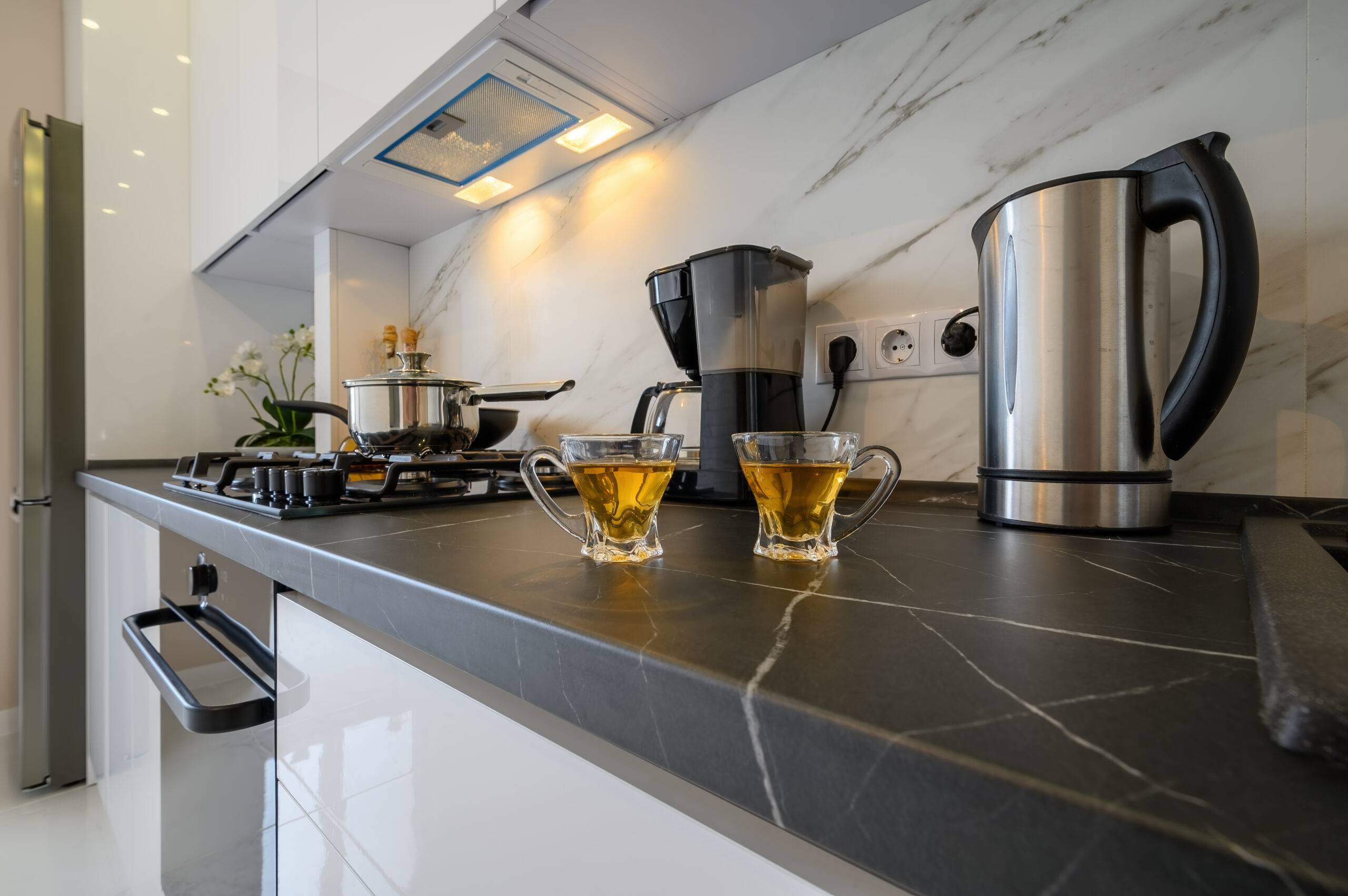 Gros plan de placard de cuisine moderne avec bouilloire électrique, cafetière et deux tasses en verre de thé