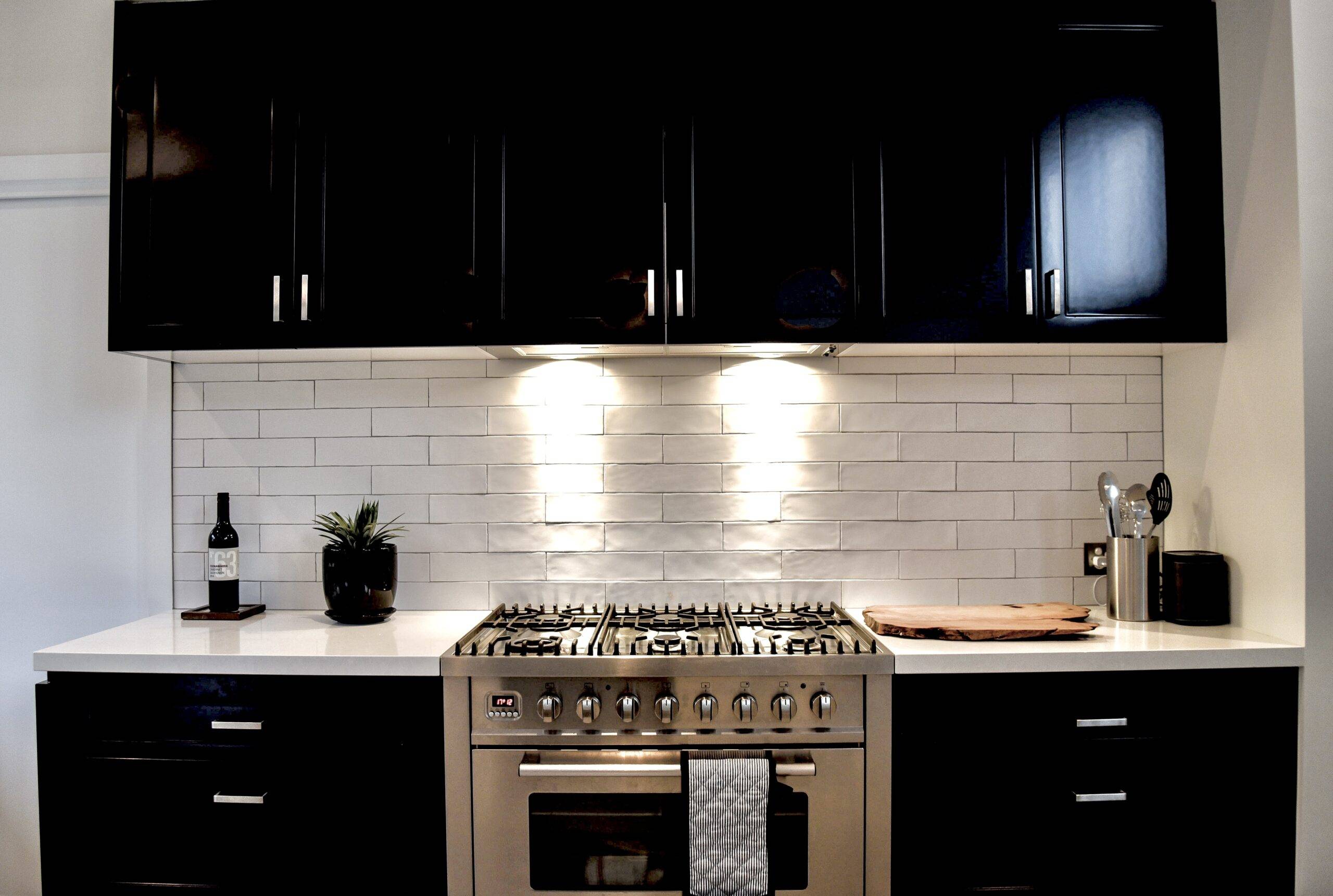 The stove and surrounding cabinets in a black and white kitchen with under-cabinet lighting.