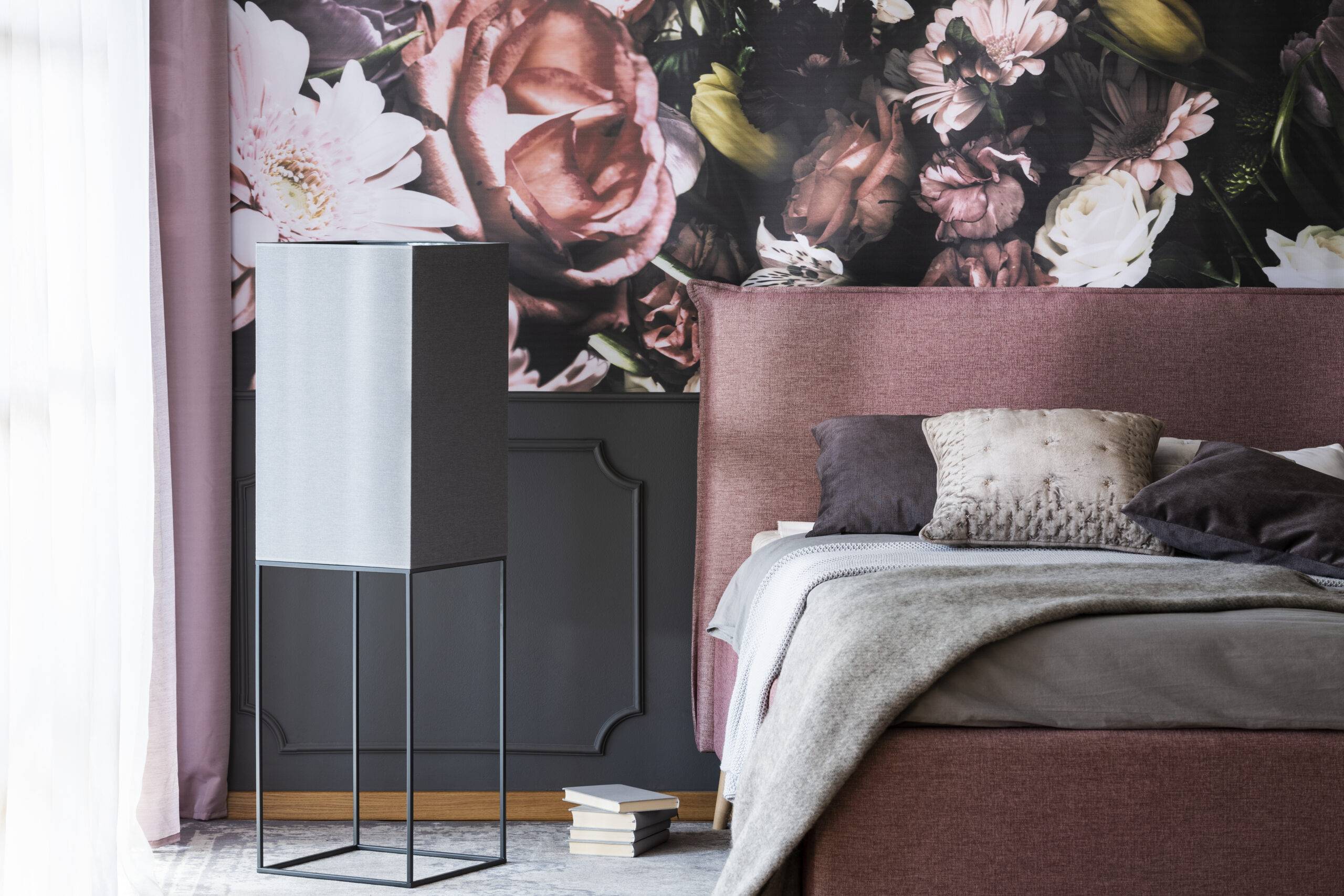 Grey pillows and bedding on bed in pink bedroom interior with flower wallpaper. Real photo