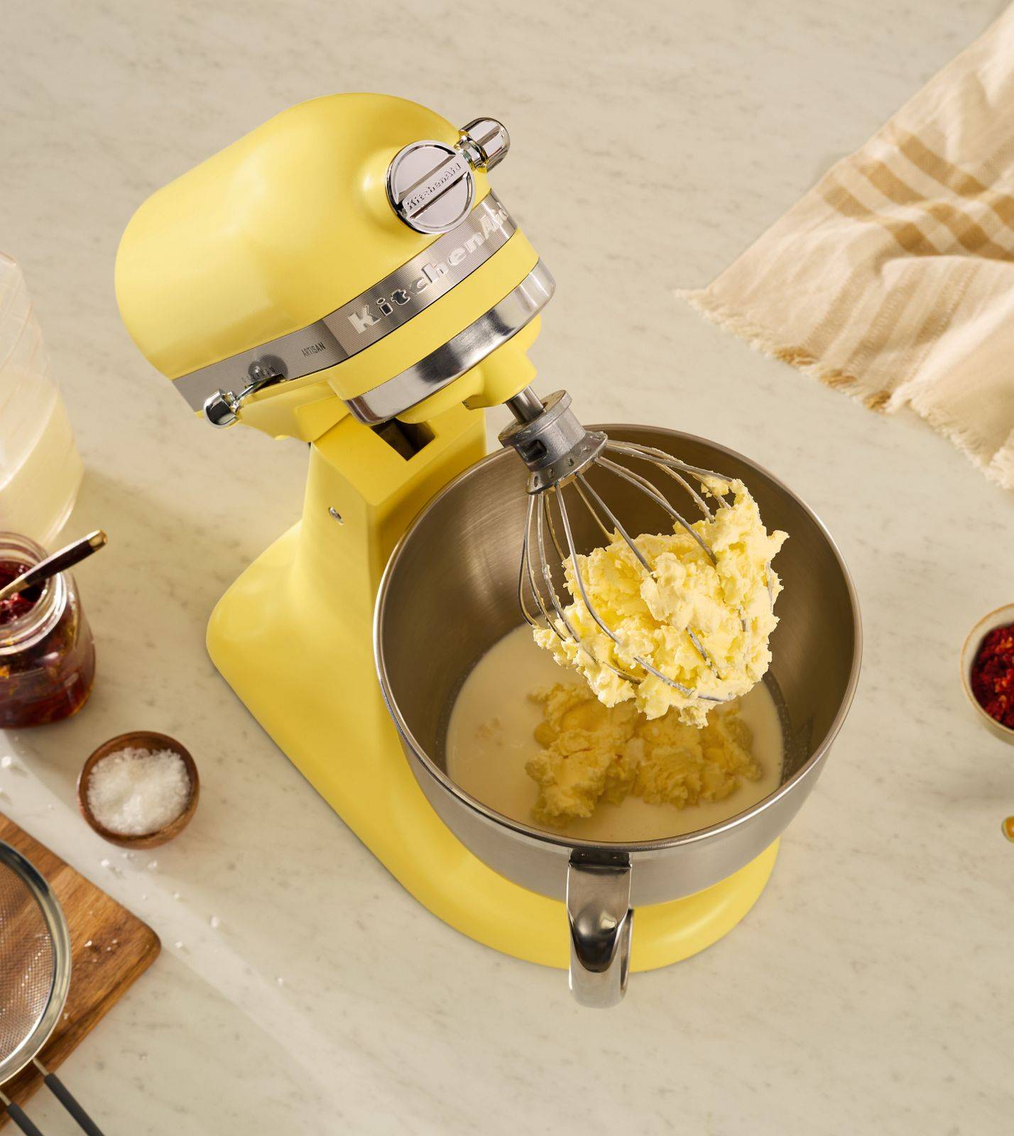 An above angle shot of a yellow kitchenaid mixer in the middle of churning some butter and buttermilk.