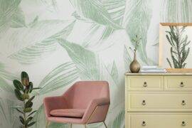 A section of a living room, zooming in on a chair and dresser with accessories, a large print leafy wallpaper behind.