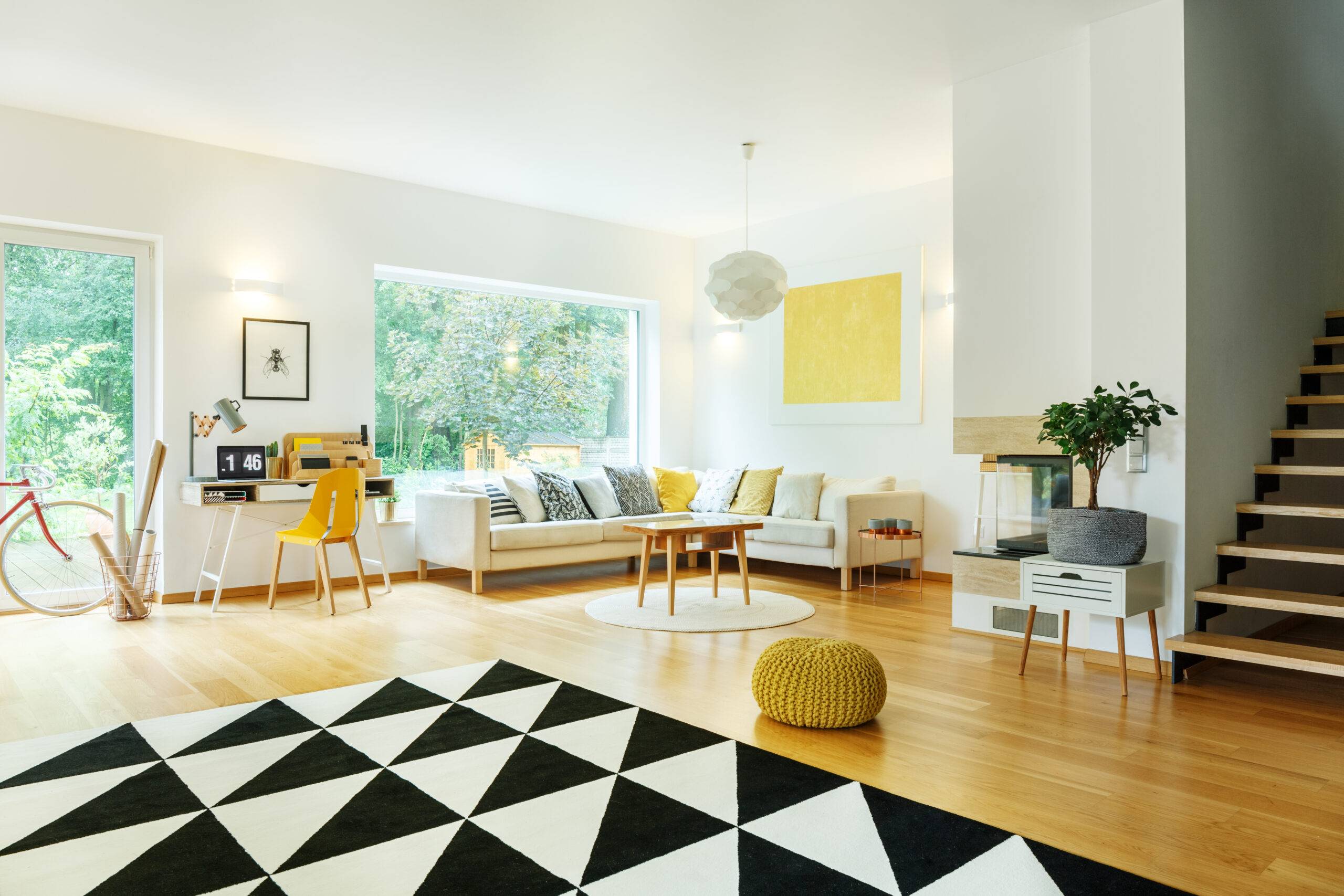 Yellow pouf and plant on cabinet in spacious apartment with corner sofa and yellow painting on wall