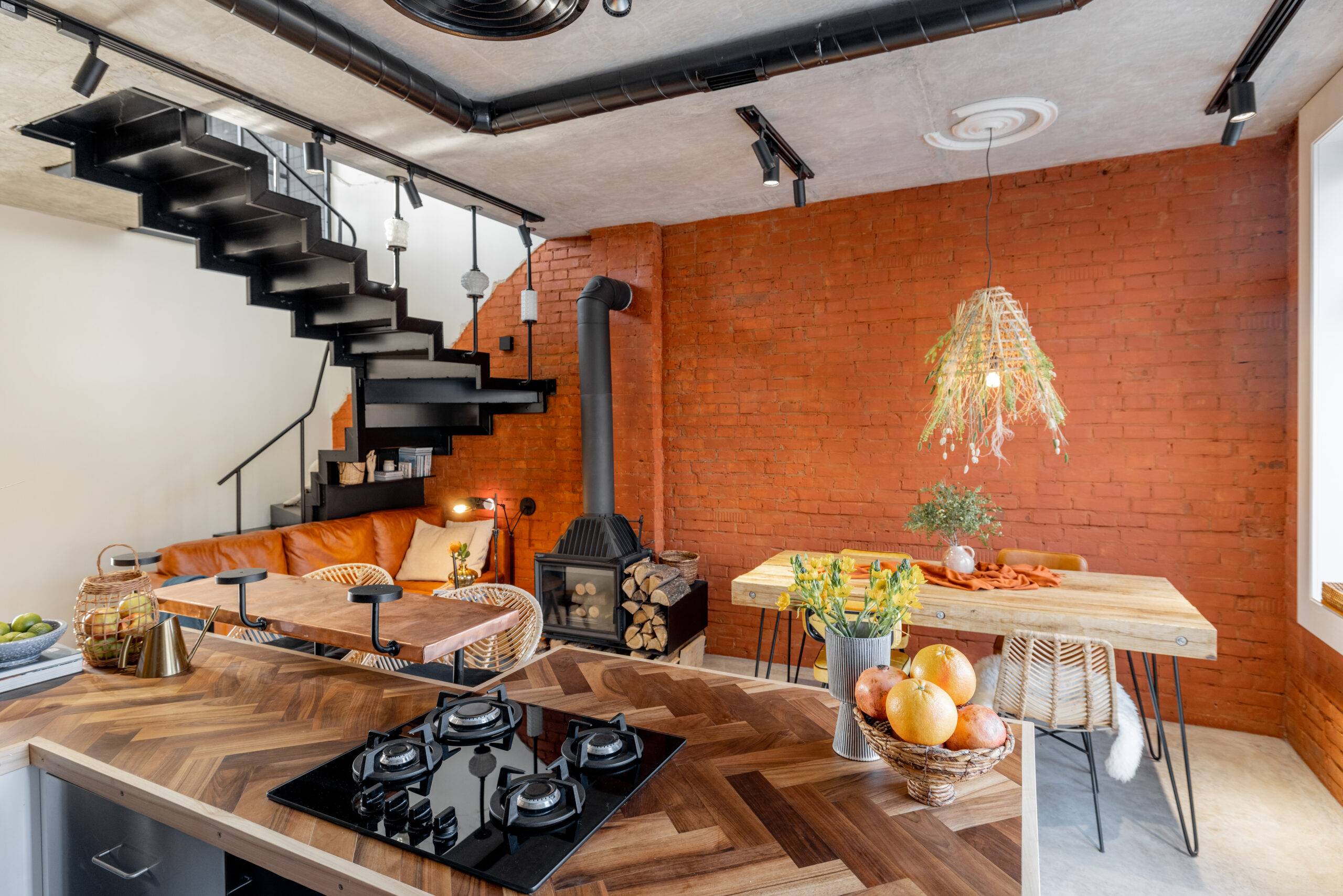 Stylish house living room interior in mixed style with the use of natural materials in finishing and furniture. Brick wall, concrete floor, ceiling, metal stairs, wooden table