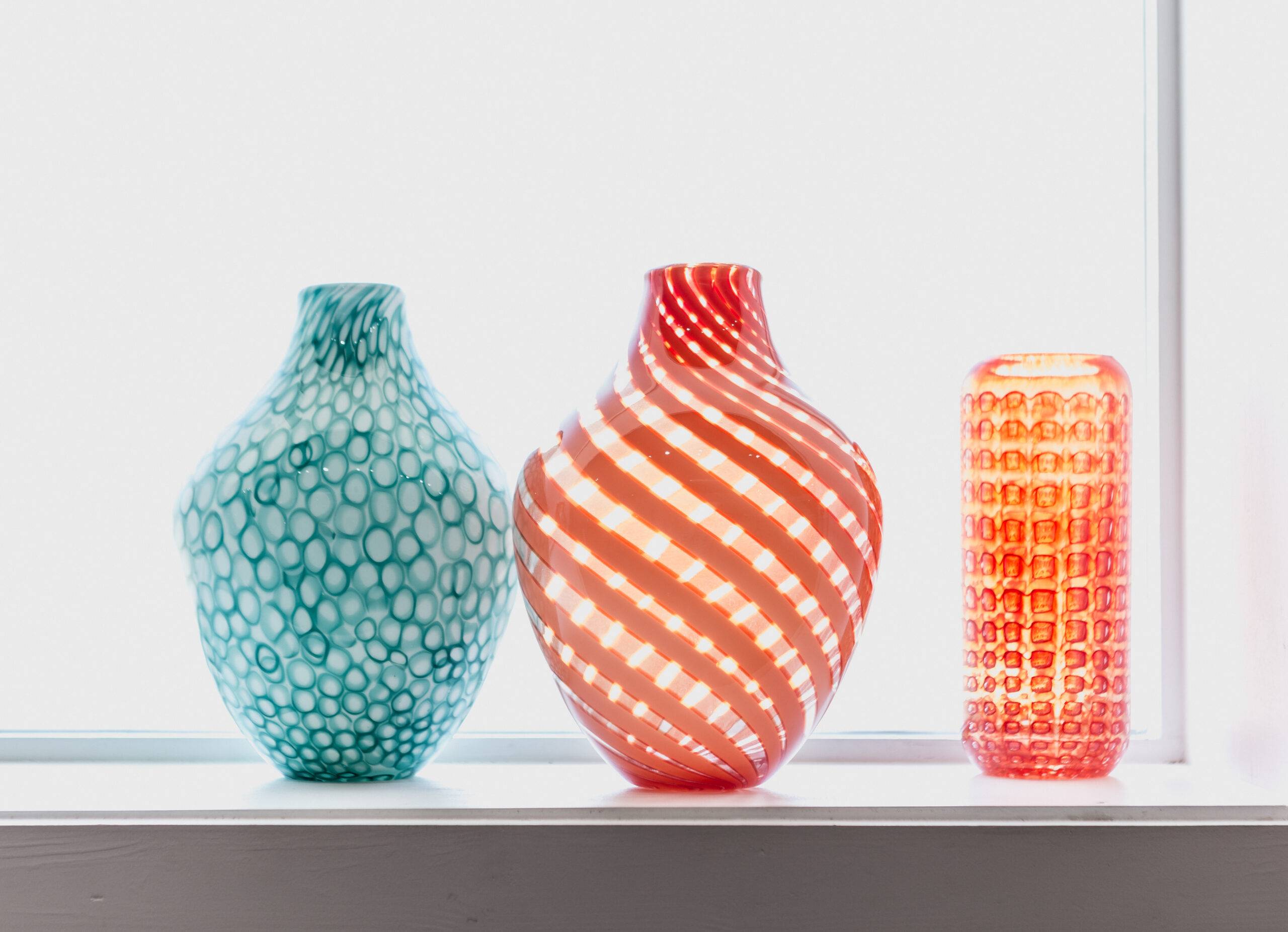 Three colorful glass vases in front of a bright window.