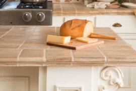 A close photo of a kitchen island with a tile countertop, a loaf of bread on a cutting board on top.