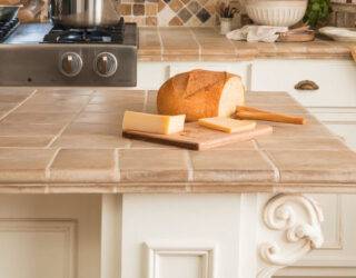 A close photo of a kitchen island with a tile countertop, a loaf of bread on a cutting board on top.