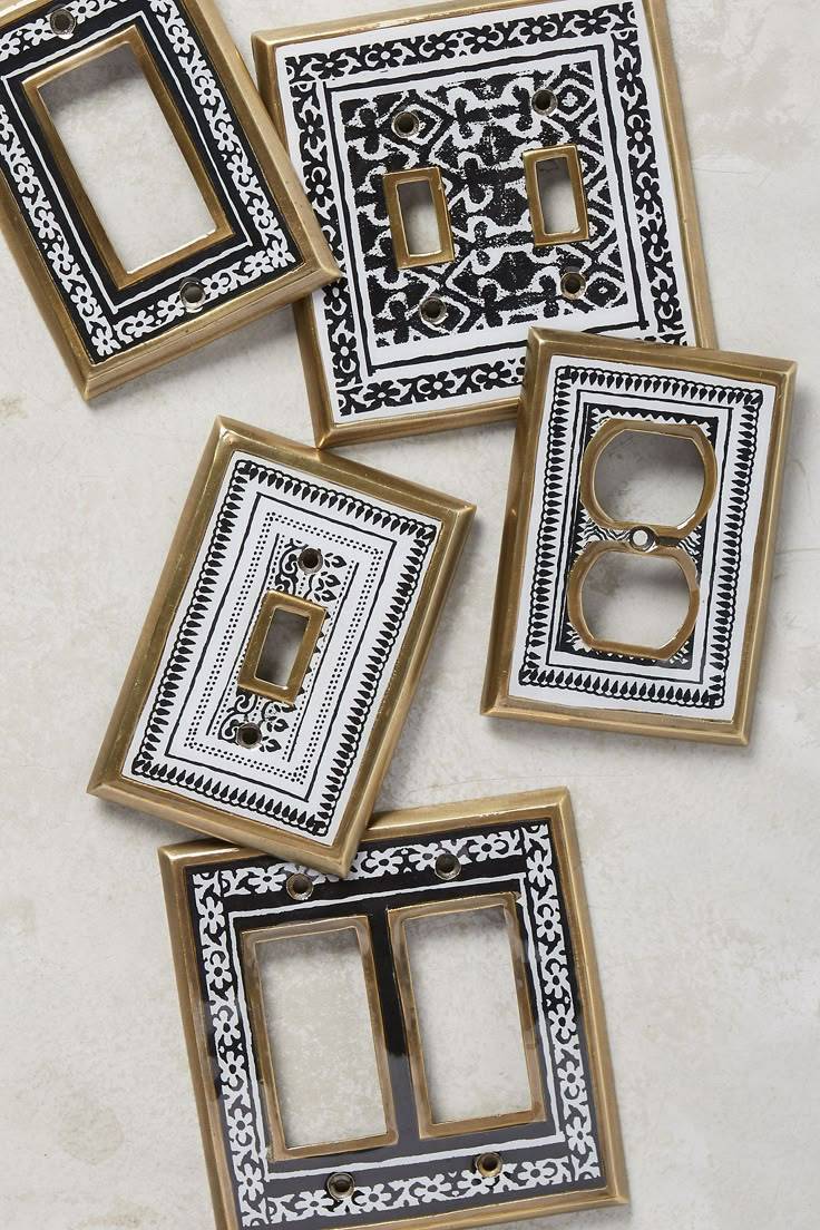 An assortment of brass light switch covers with black and white patterns painted on it.