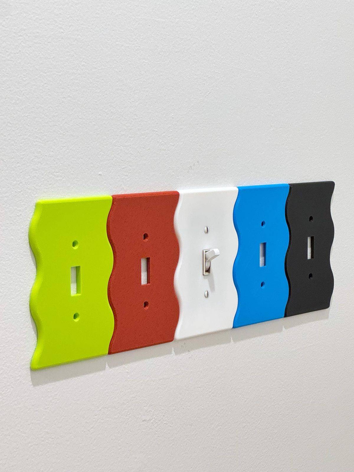 Five wavy light switch covers all lined up next to  one another on the wall.