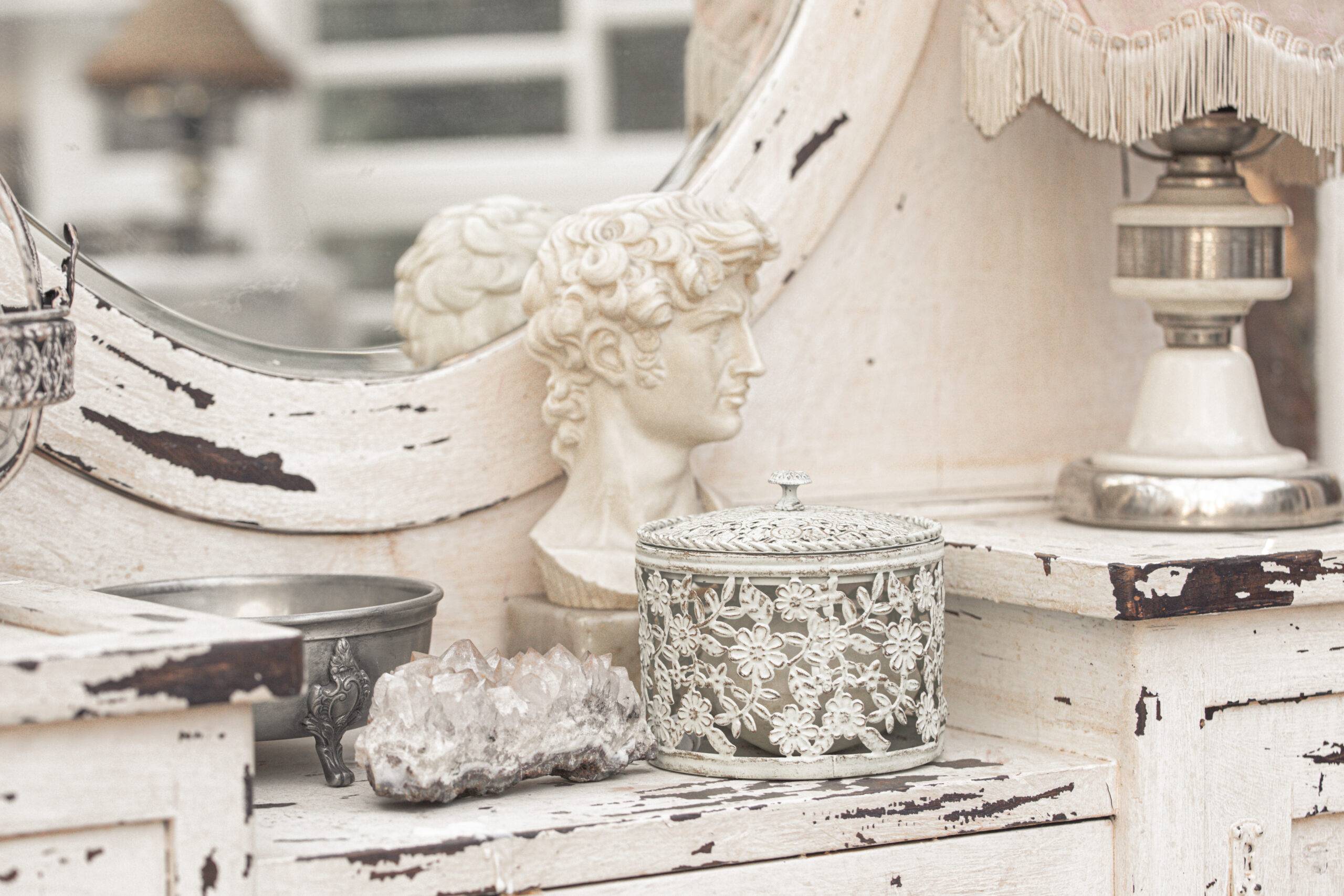 Cosmetics on white vintage dressing table with retro lamp, crystals in light white shabby chic vintage french Provence country interior room with wooden painted furniture and antique objects