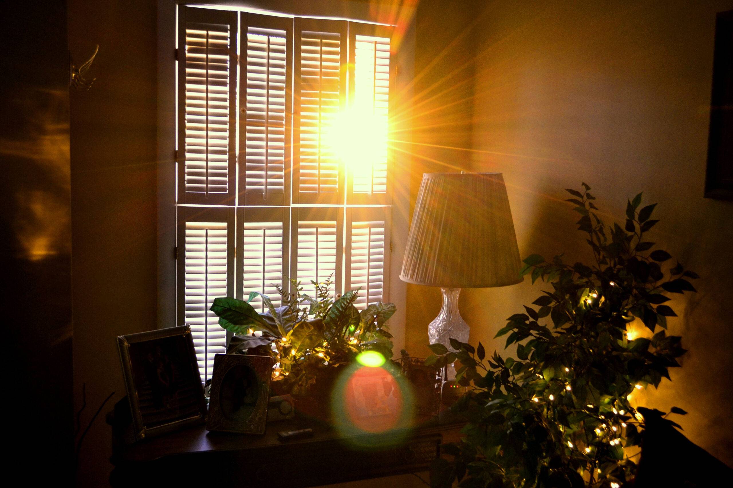 The sunlight shining into a room through semi-open blinds.