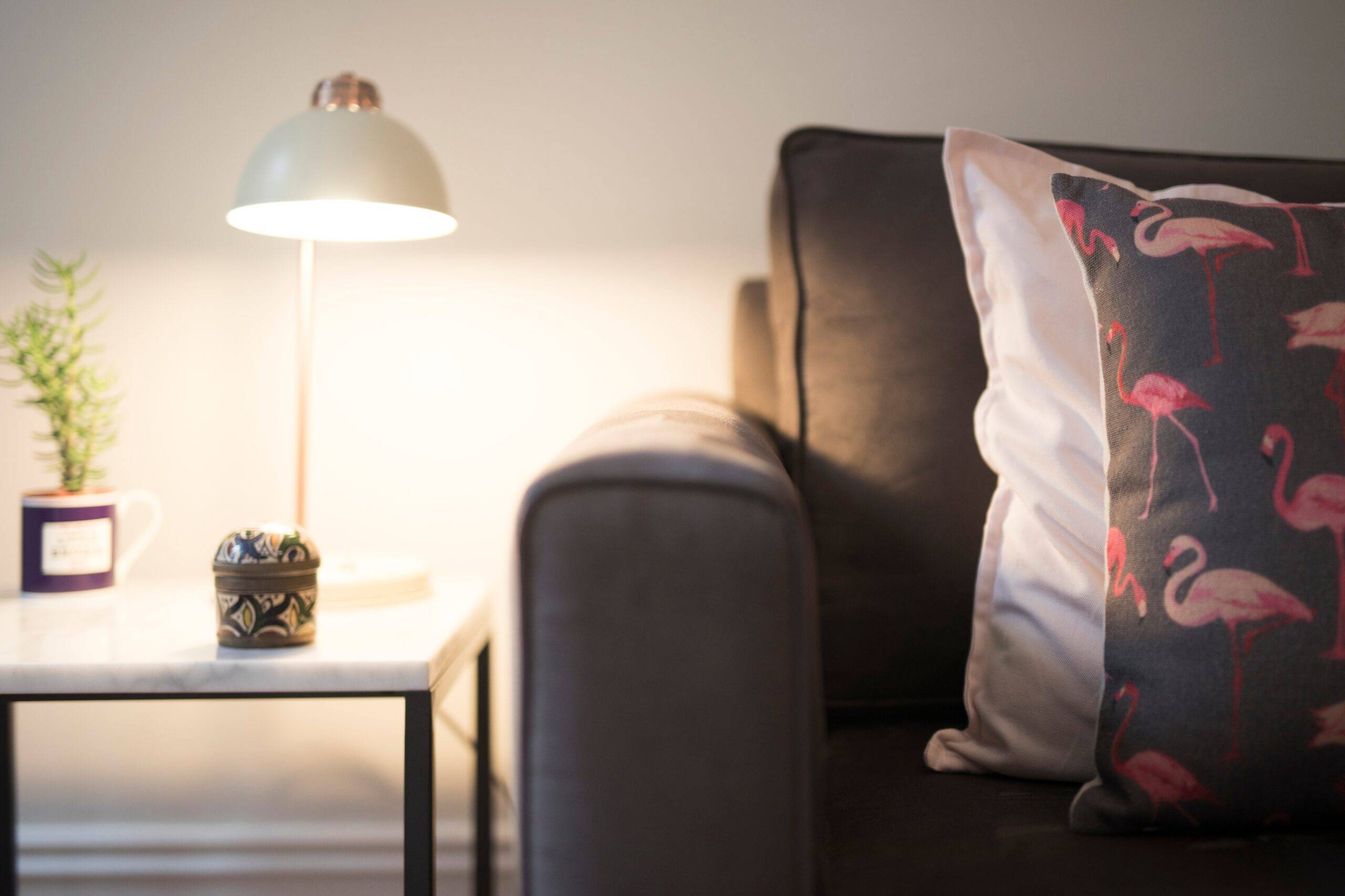 A table lamp shining on a side table next to a couch.