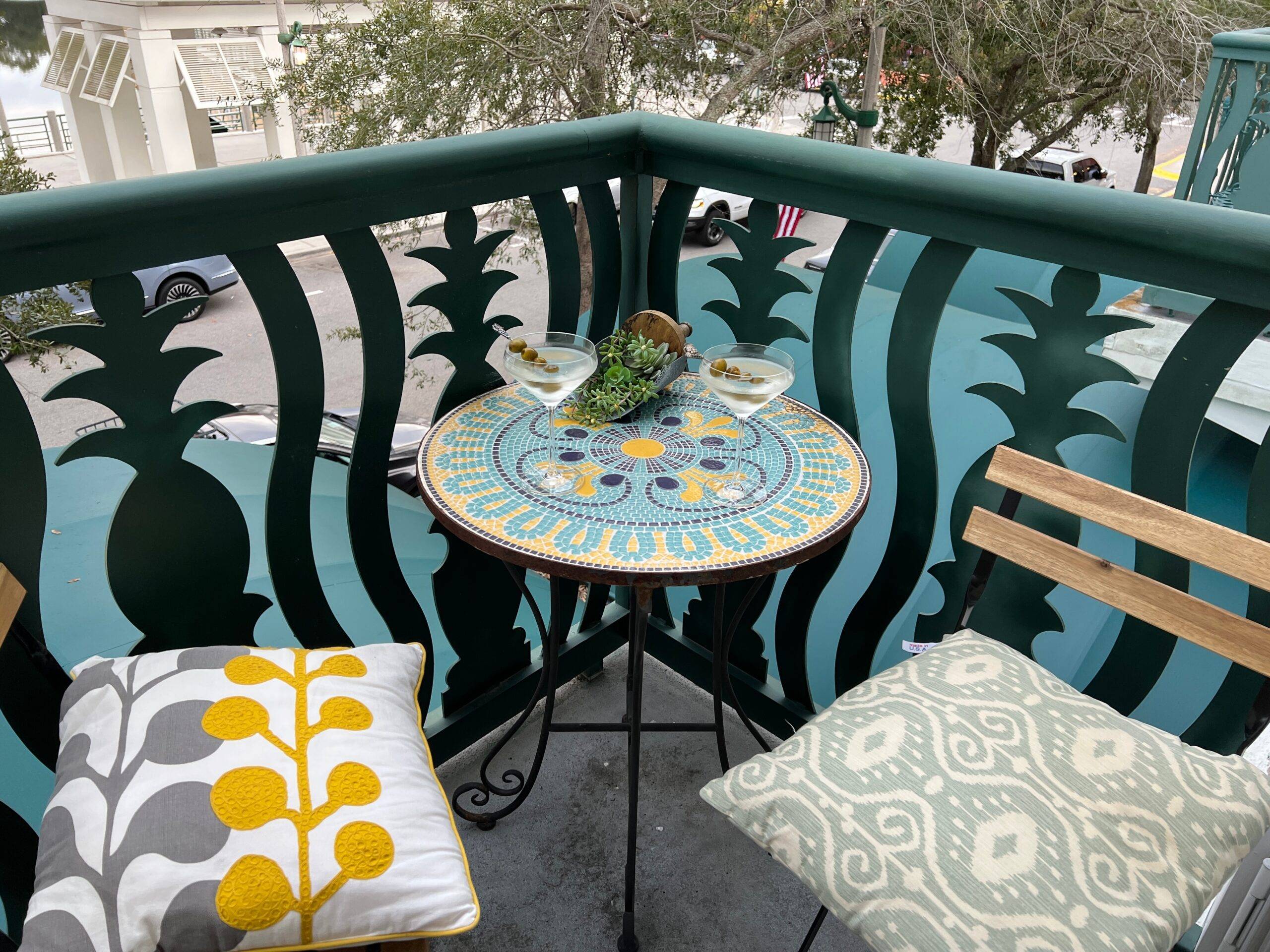 A small table and two chairs with colorful cushions on a bacony.