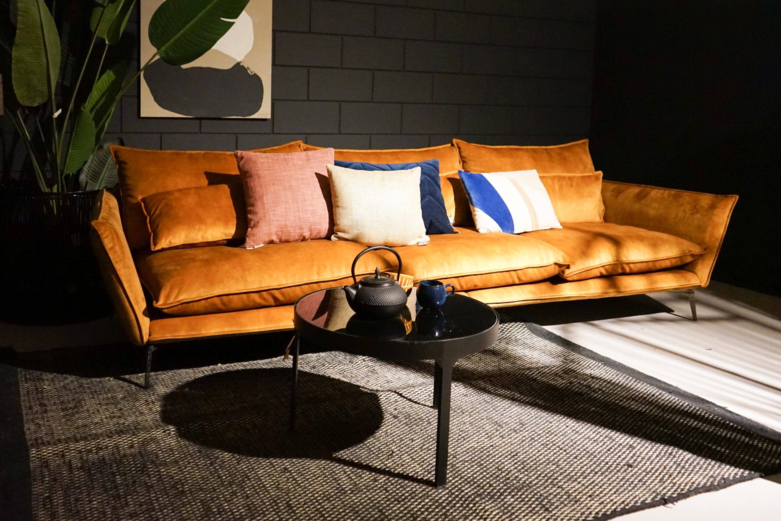 An orange couch in a dark living room with a spot of sunlight shining on it.