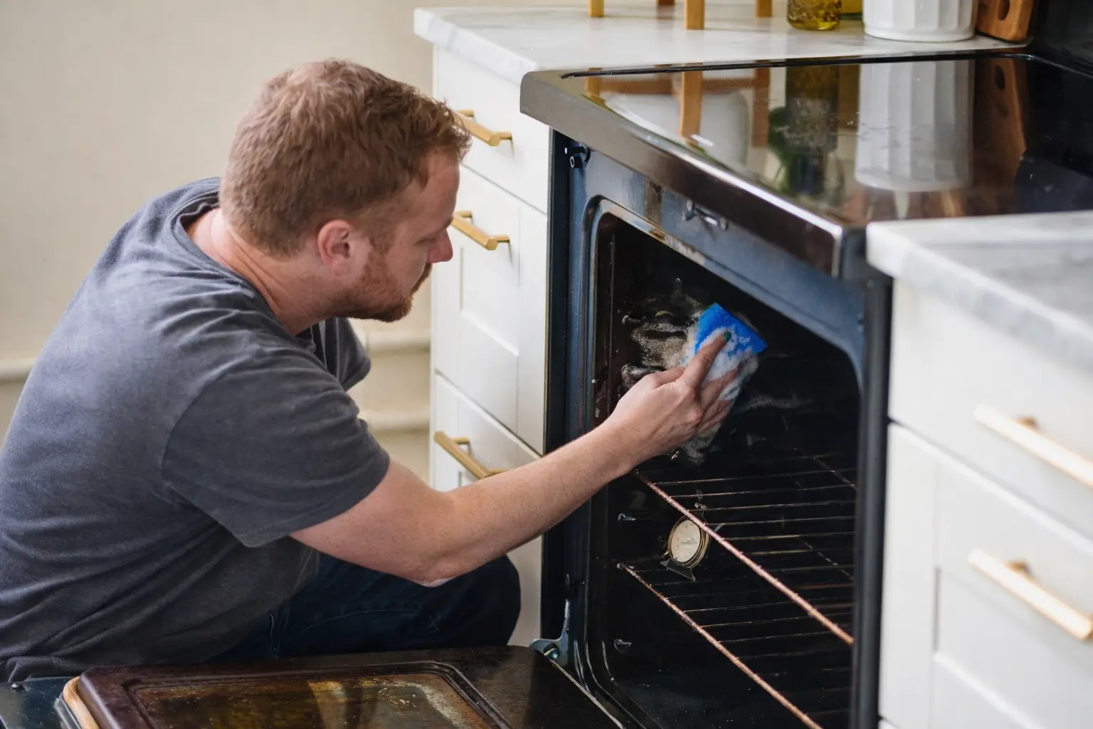 An image of a person cleaning the insides of their oven while crouched.