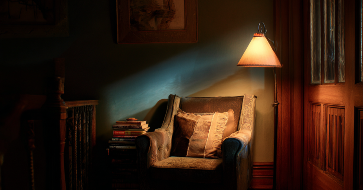 Cinematic shot of a reading nook in a home, with a floor lamp pooling warm light over the seat.